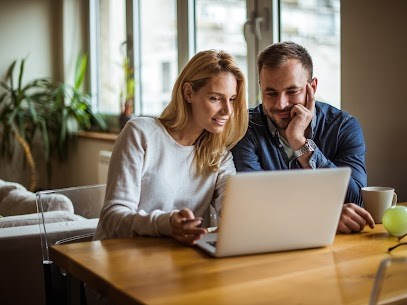 A man and woman sitting on a desk looking at a laptop