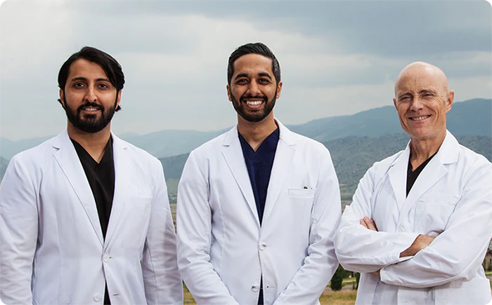 A photo of three Wyndly doctors wearing white coats posing outside with mountains int he background