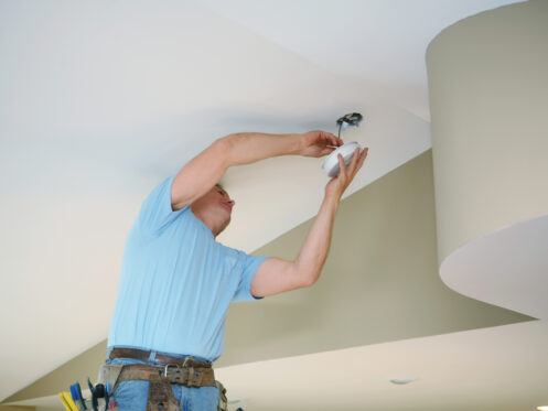 Technician removing a smoke alarm on the ceiling inside a home