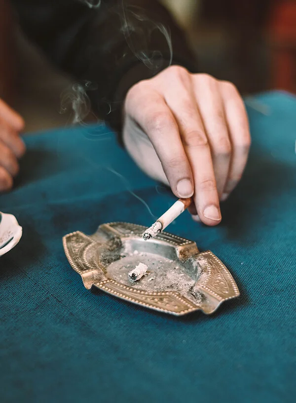 A hand holding a cigarette against an ashtray on a green table
