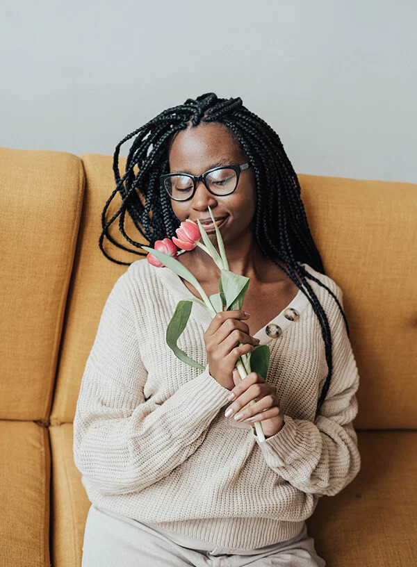 Woman sitting on a couch and smelling pink roses and looking happy and relieved