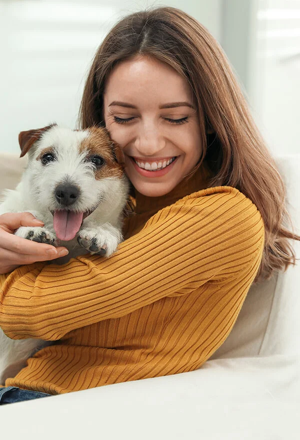 Happy woman with yellow sweater holding her dog while sitting on couch