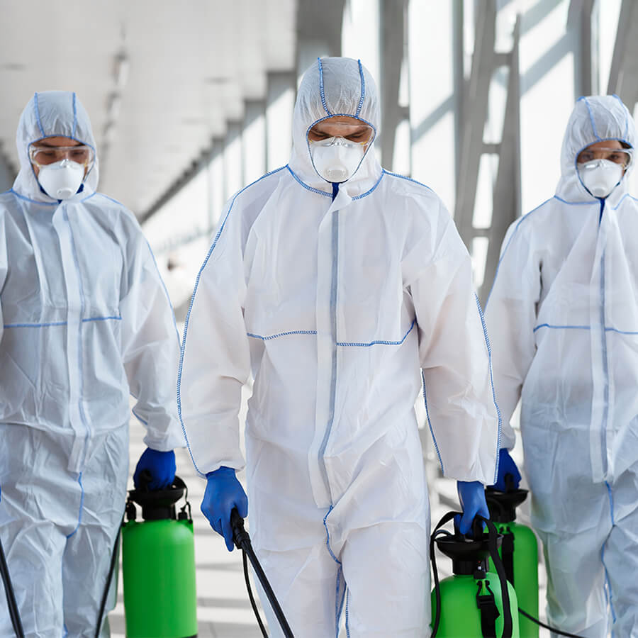 Three technicians in hazmat suites holding equipment walking together side-by-side