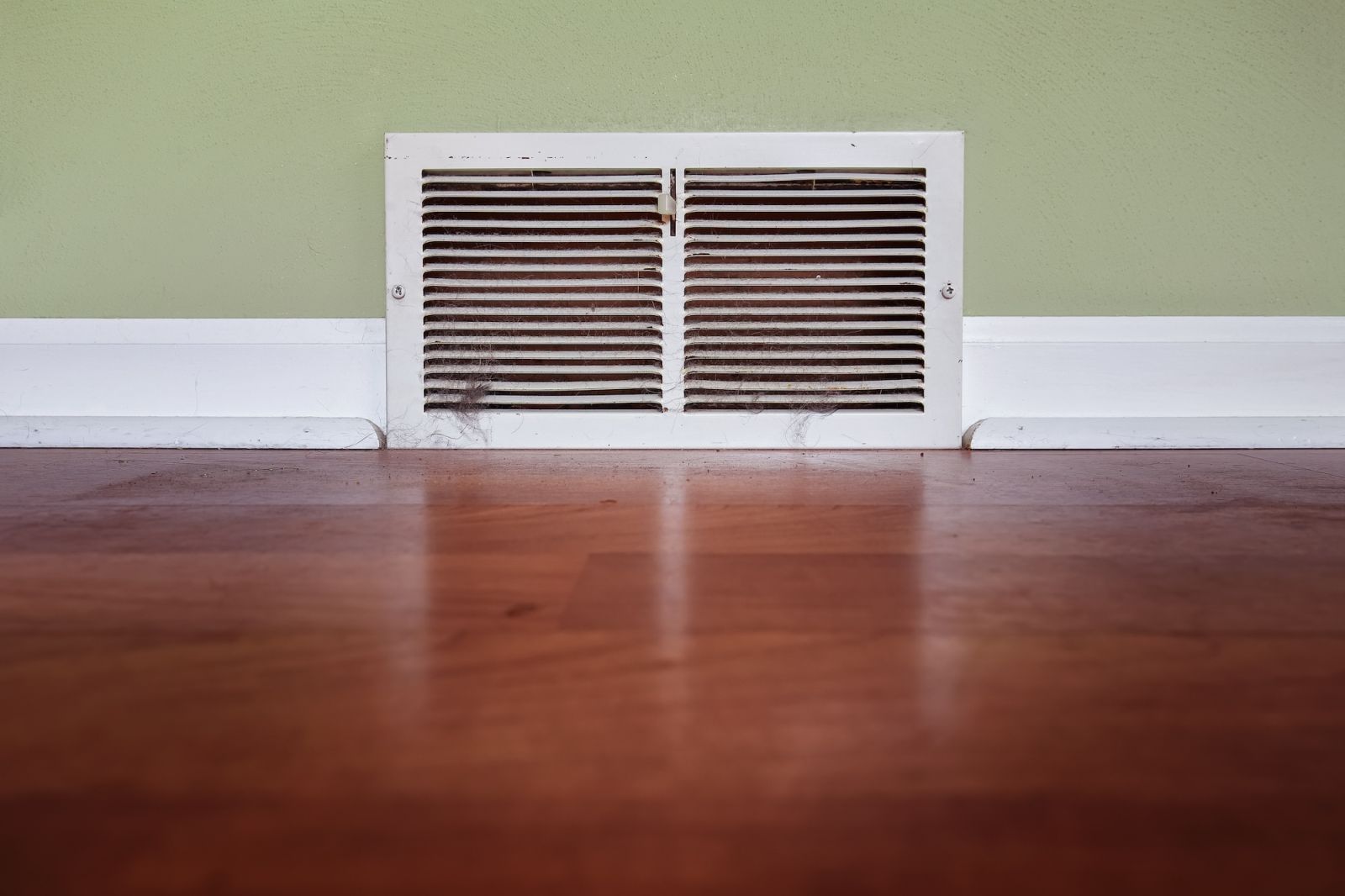 Dirty register wall vent with dust and pet hair clogging the duct opening in a home